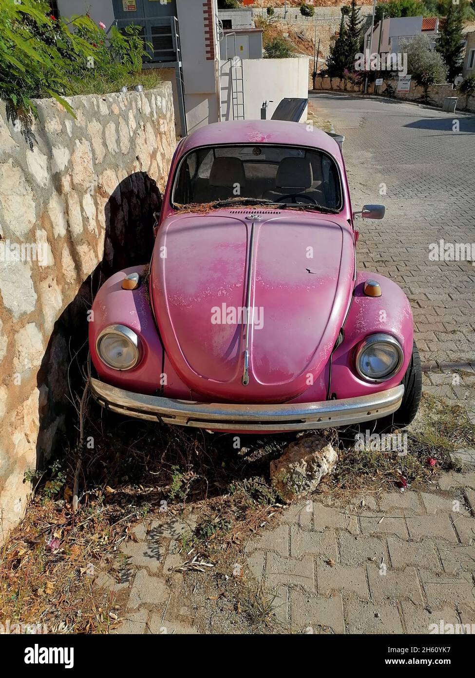 Verlassene rosa Volkswagen Beetle Auto auf der Straße in der Nähe der Steinmauer geparkt. Stockfoto