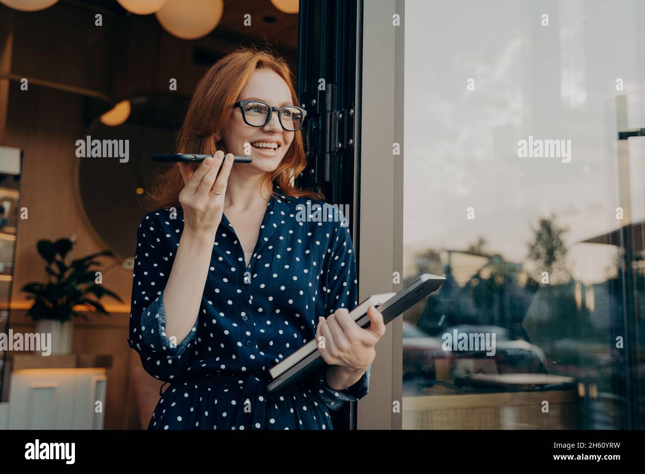 Glückliche Geschäftsfrau, Freiberuflerin mit Laptop, hält Mobiltelefon und spricht über eine Freisprecheinrichtung Stockfoto