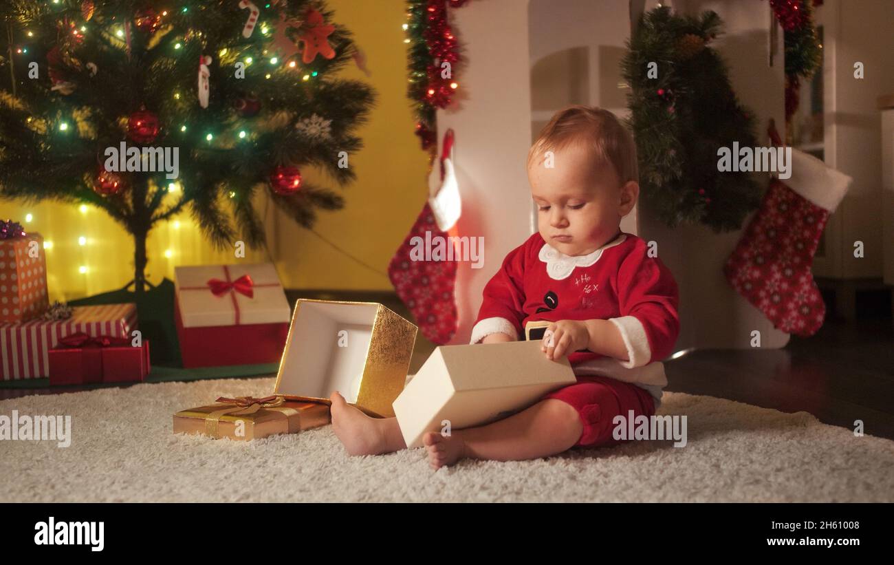 Kleiner Junge spielt mit Weihnachtsgeschenk-Box und bunten dekorativen Kugeln. Familien und Kinder feiern Winterferien. Stockfoto