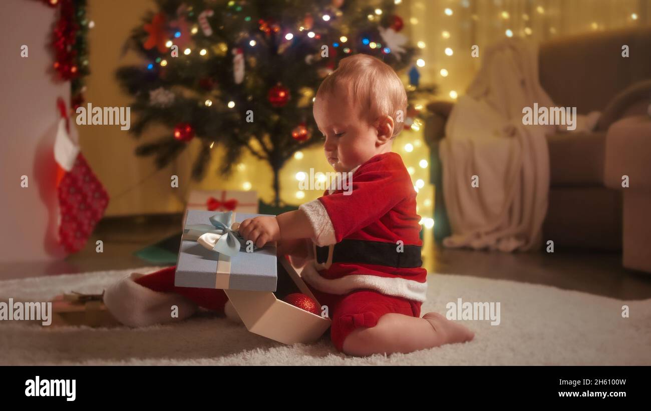 Kleiner Junge im Weihnachtsmann Kostüm Auspacken und in die Box schauen mit Weihnachtsgeschenken und Geschenken Stockfoto