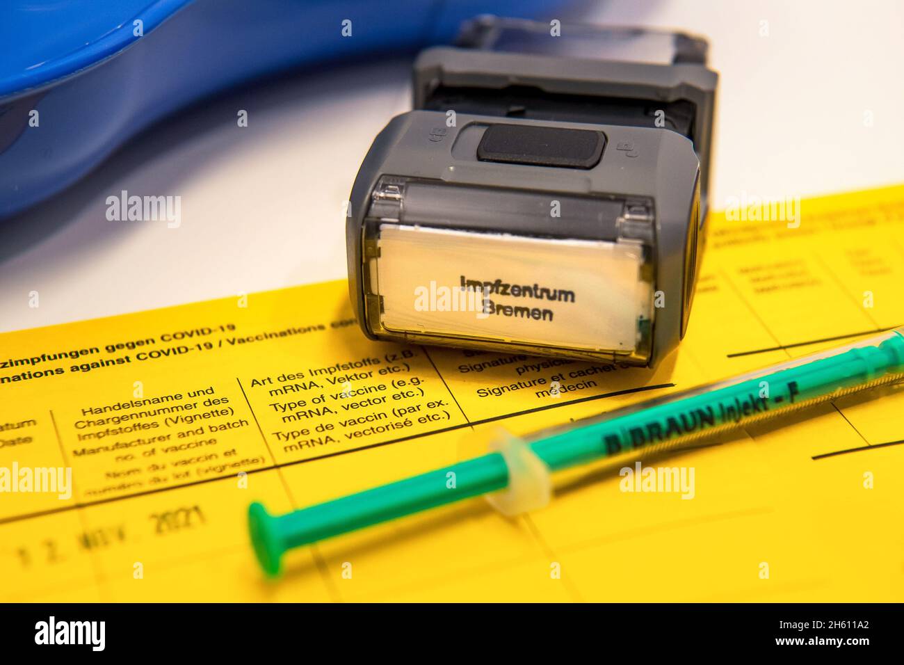 Bremen, Deutschland. November 2021. ABBILDUNG - Ein Stempel des Impfzentrums Bremen liegt neben einer Spritze auf einem Impfpass des Impfzentrums Bremen West. Das Land Bremen hat nach wie vor die höchste Rate an Corona-Impfungen im Ländervergleich. Quelle: Sina Schuldt/dpa/Alamy Live News Stockfoto