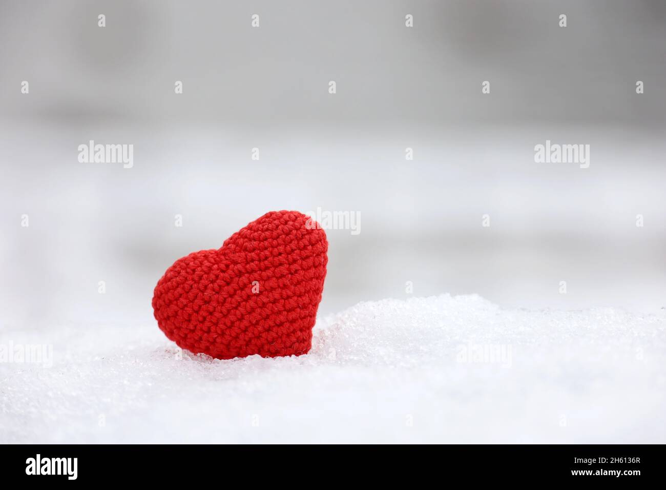 Rot gestricktes Herz im Schnee mit verschwommenem Naturhintergrund. Valentinskarte, Symbol der Liebe, romantisches Ereignis im Winter, Weihnachtsfeier Stockfoto
