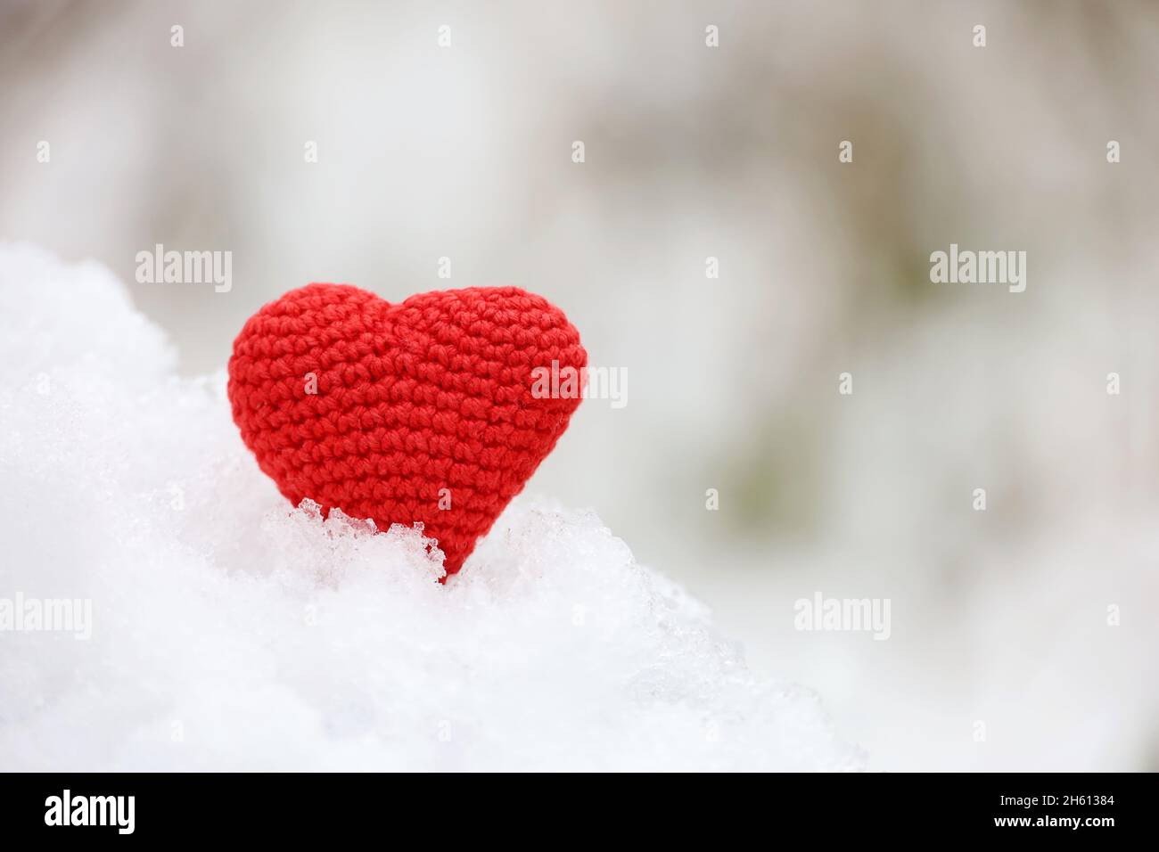 Rot gestricktes Herz im Schnee mit verschwommenem Naturhintergrund. Valentinskarte, Symbol der Liebe, romantisches Ereignis im Winter, Weihnachtsfeier Stockfoto