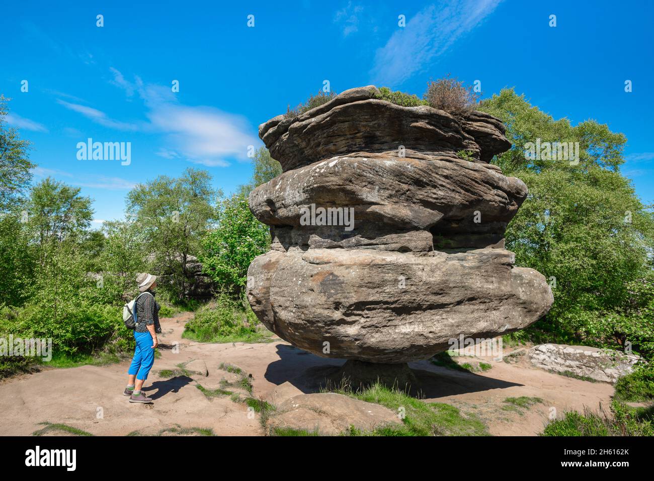Idol Rock, Blick im Sommer auf eine Frau mittleren Alters, die Idol Rock, eine riesige erodierte Felsformation, die auf ihrer eigenen Achse ausgeglichen ist, Brimham Rocks, Yorkshire, anschaut Stockfoto