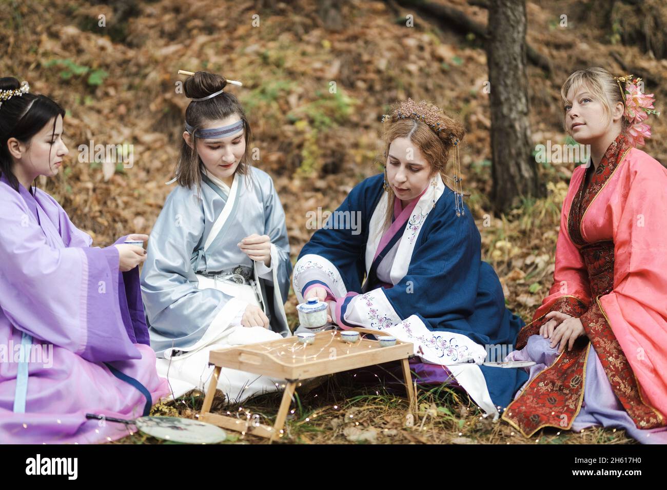 Vier Frauen in traditionellen chinesischen Hanfu-Kleidern trinken Tee mitten in einem Wald Stockfoto