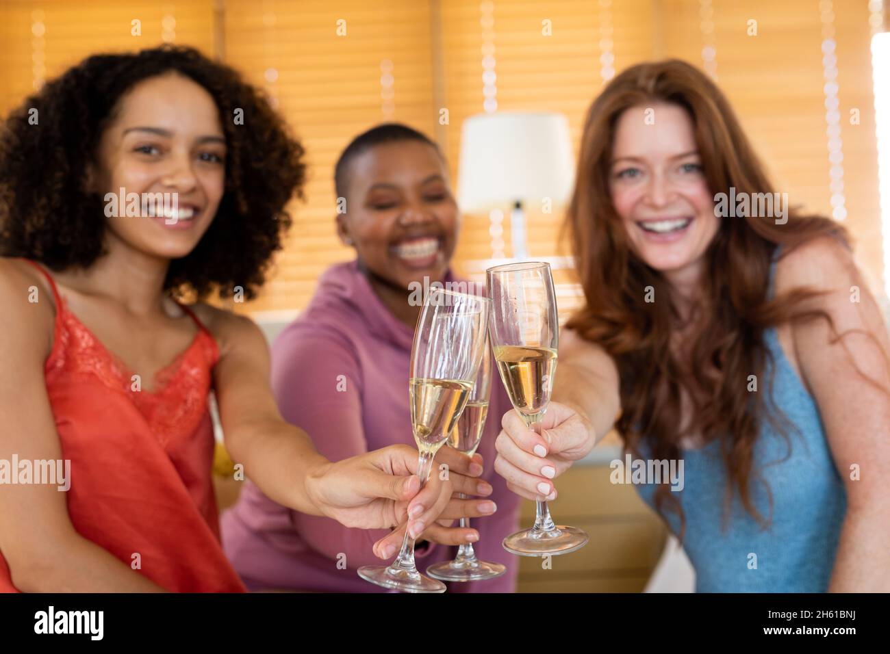 Glückliche multirassische Freundinnen, die während der Hausfeier Champagner-Flöten toasten Stockfoto