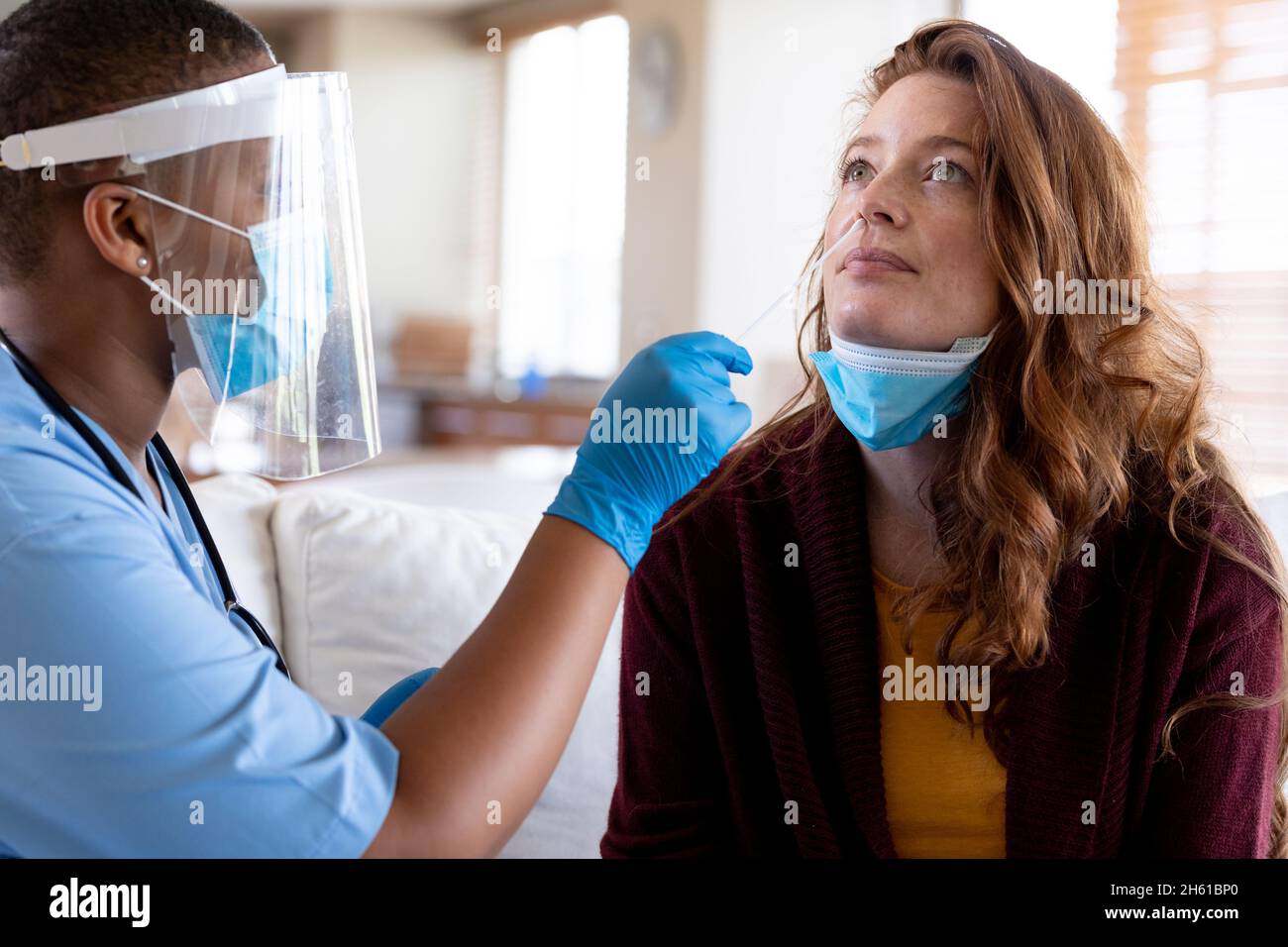 Ärztin in schützender Gesichtsmaske, die während des Covid-19-Ausbruchs einen Abstrichtest der Frau in der Klinik abnahm Stockfoto