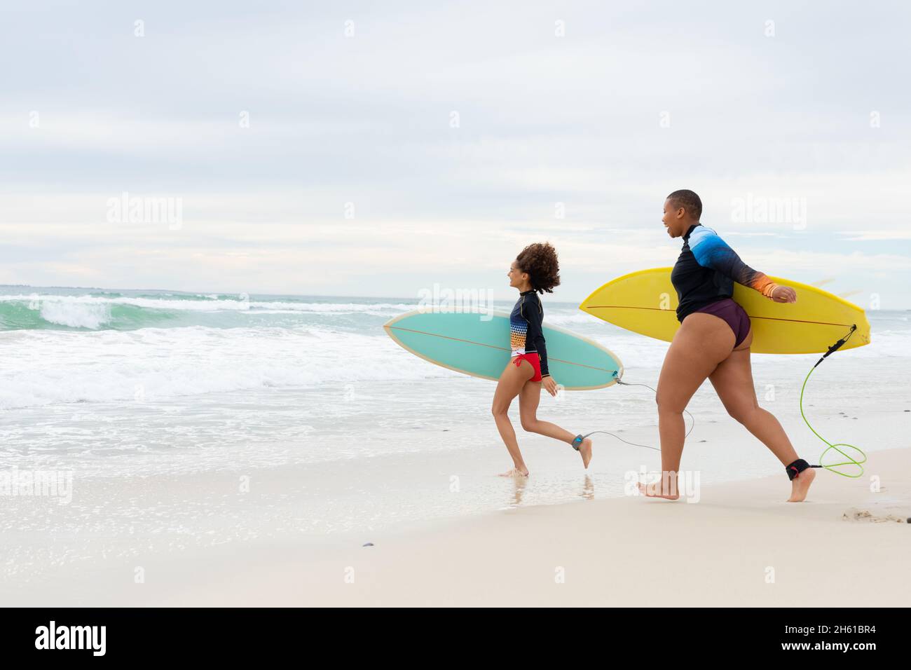 Die ganze Länge von sorglosen multirassischen Freundinnen mit Surfbrettern, die am Wochenende am Strand laufen Stockfoto