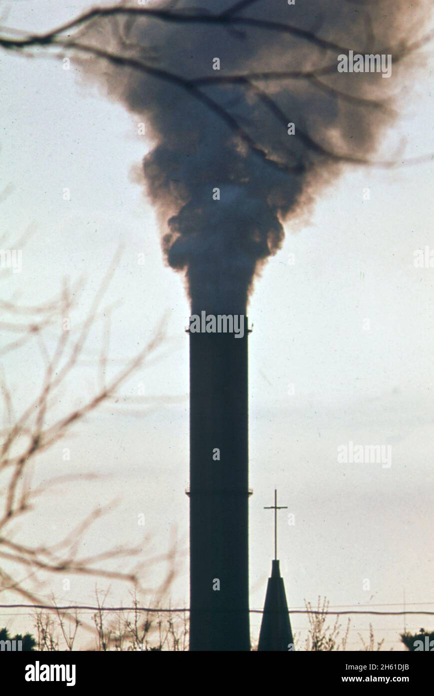 Der Rauchschornstein der Kaiser-Aluminium-Fabrik, hinter der katholischen Kirche, schellt Dämpfe über dem großen Wohngebiet im Chalmette-Teil von New Orleans Ca. März 1973 Stockfoto