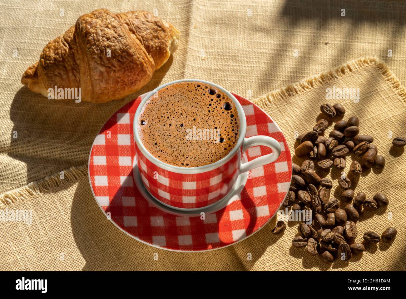 Tasse Kaffee, Croissant und Kaffeebohnen, beleuchtet vom Sonnenlicht, Herbsttag. Stockfoto