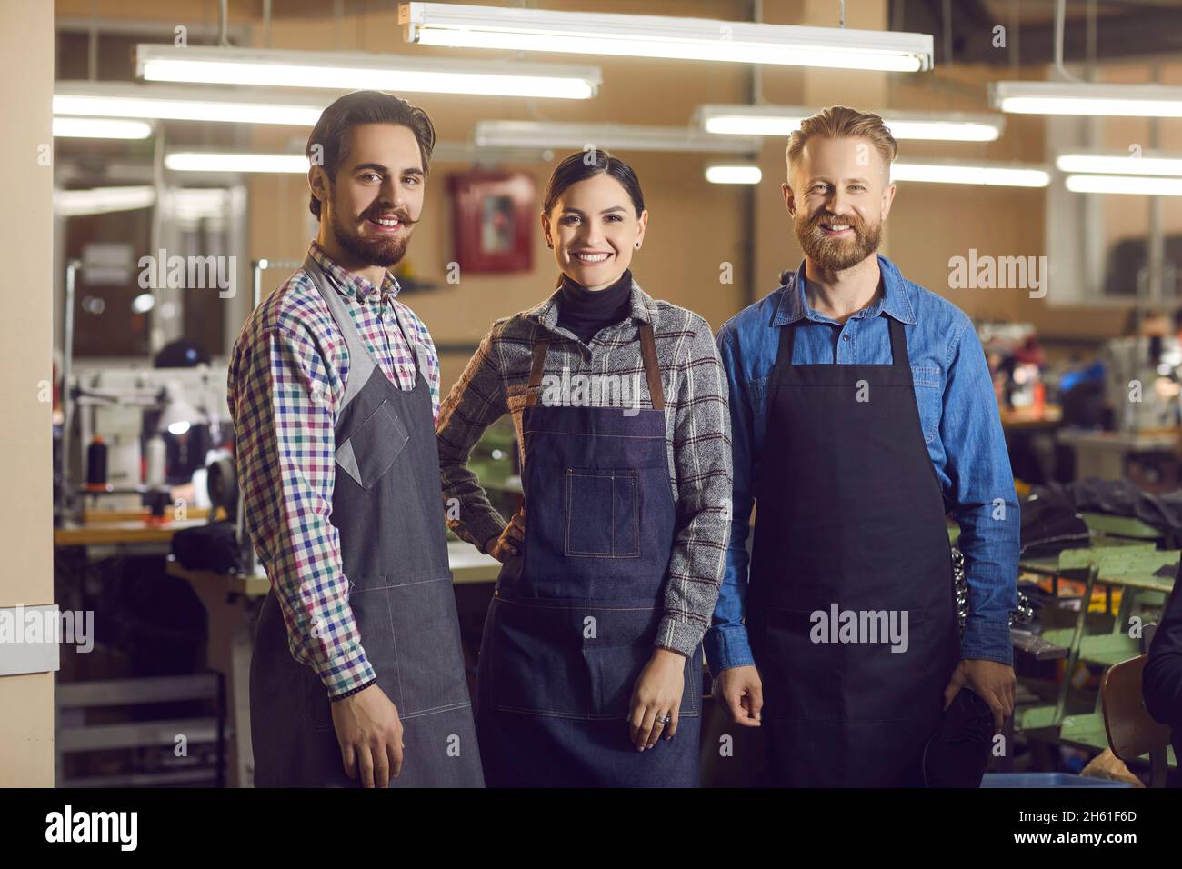 Porträt von drei kaukasischen erfahrenen lächelnden Arbeitern in der Schuh- und Bekleidungsfabrik bei der Arbeit. Stockfoto