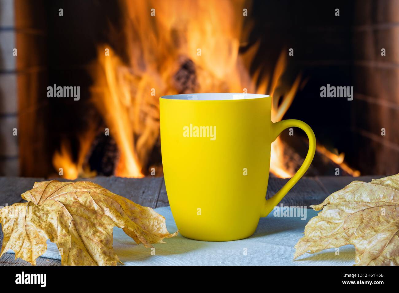 Gelbe Tasse Tee oder Kaffee vor einem gemütlichen Kamin, in einem Landhaus, Herbst- oder Winterferien, horizontal. Stockfoto