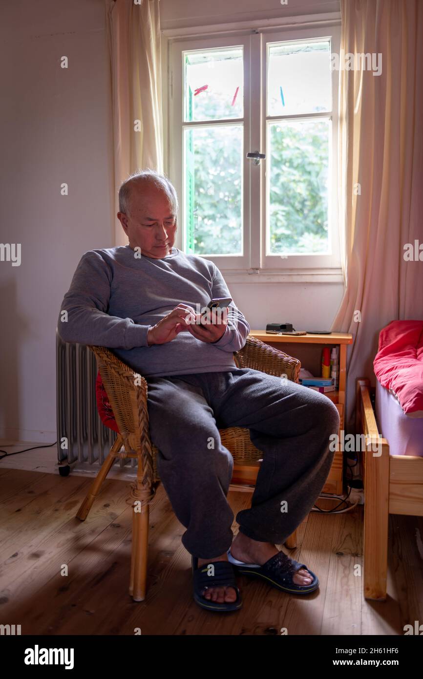 Ein gereifter Mann, der sich zu Hause entspannt und auf einem bequemen Stuhl am Fenster sitzt. Stockfoto