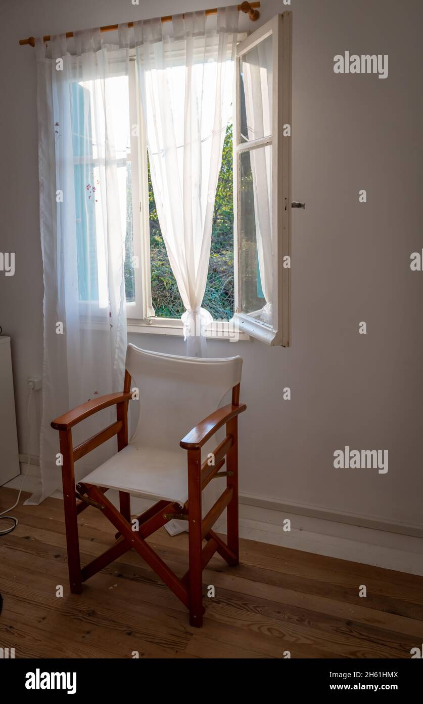 Innenraum eines Raumes mit einem Regiestuhl an einem geöffneten Fenster. Stockfoto