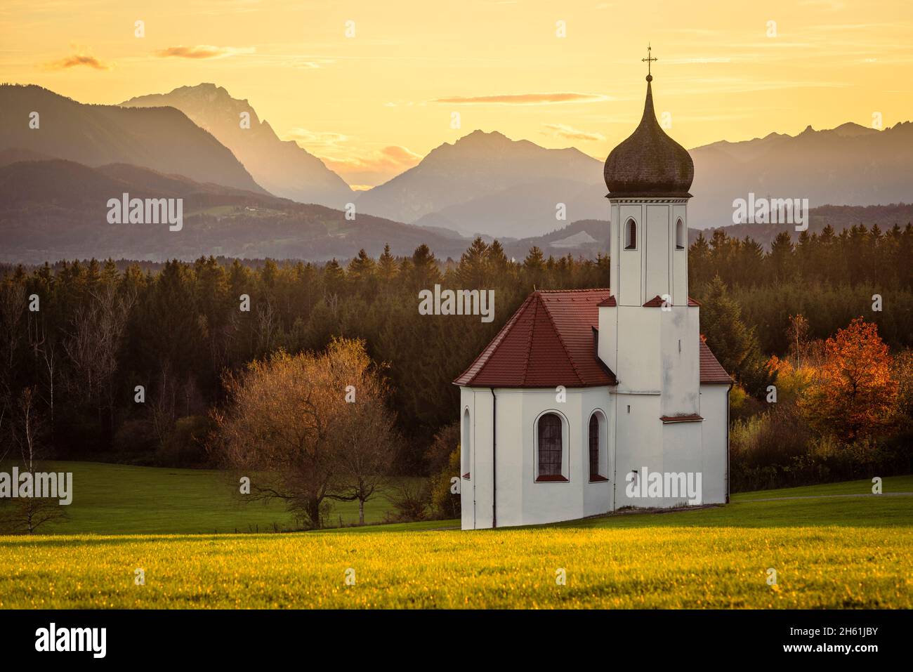 Die Barockkapelle St. Johann über dem Loisachtal und die herbstlichen bayerischen Alpen mit Zugspitze in der Abendsonne, Deutschland Stockfoto