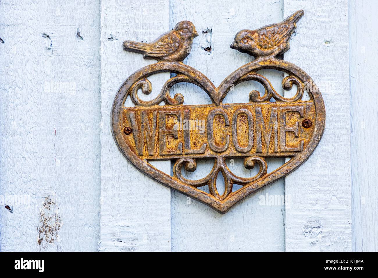 Willkommenstafel aus Gusseisen mit Herz und zwei Vögeln an einer Holztür Stockfoto