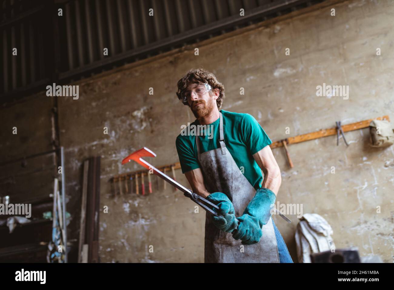 Kaukasischer Schmied in Schutzbrillen und Handschuhschmieden in der Metallindustrie Stockfoto