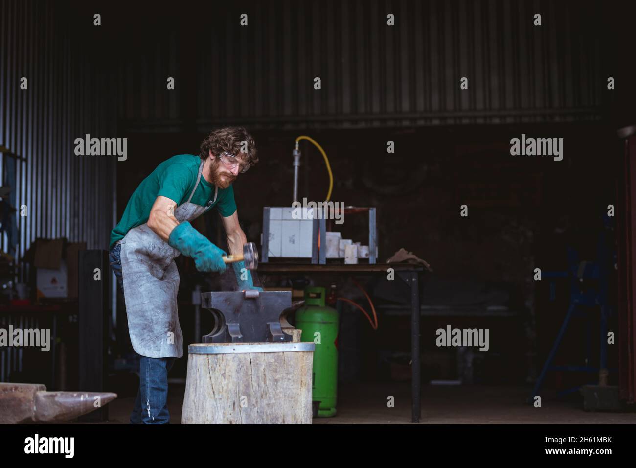 Kaukasischer Schmied in der Arbeitsschutzschmiede mit Hammer auf Amboss in der Industrie Stockfoto