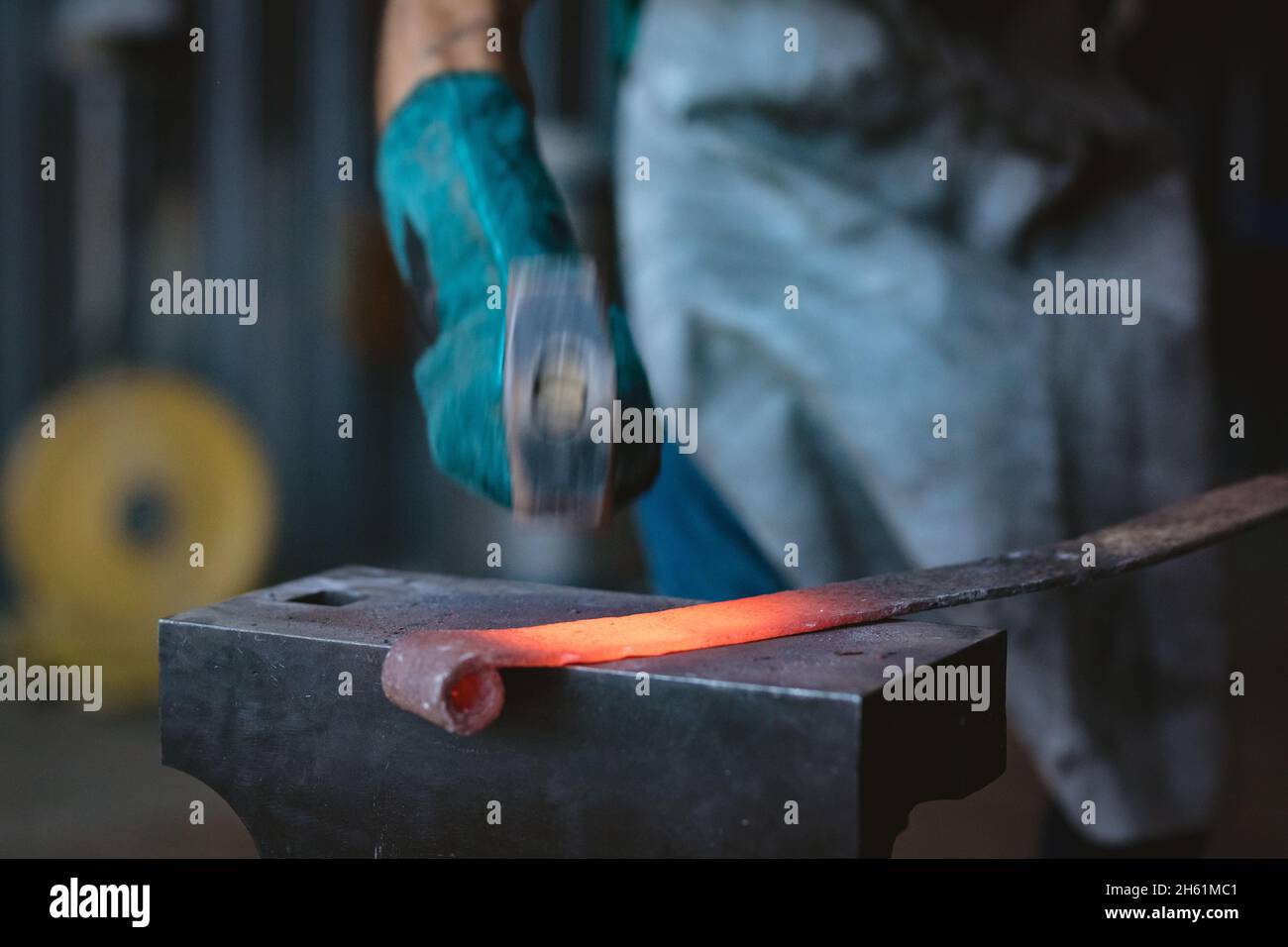 Zugeschnittenes Bild des Schmieds in der Industrie beim Schmieden von Schutzhandschuhen mit Hammer auf Amboss Stockfoto