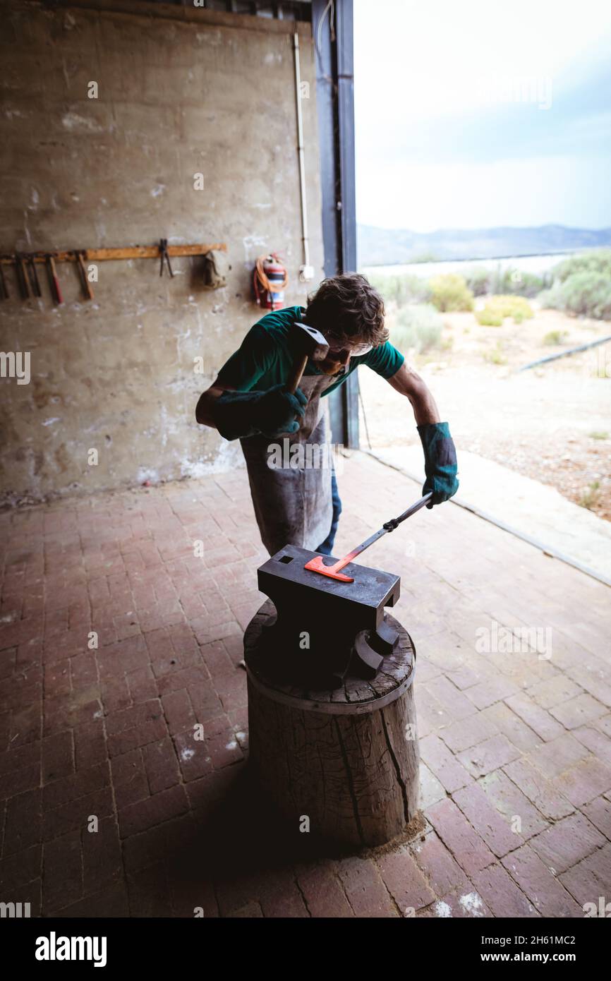 Schmied in Schutzarbeitsverschleißschmieden mit Hammer auf Amboss in der Fertigungsindustrie Stockfoto