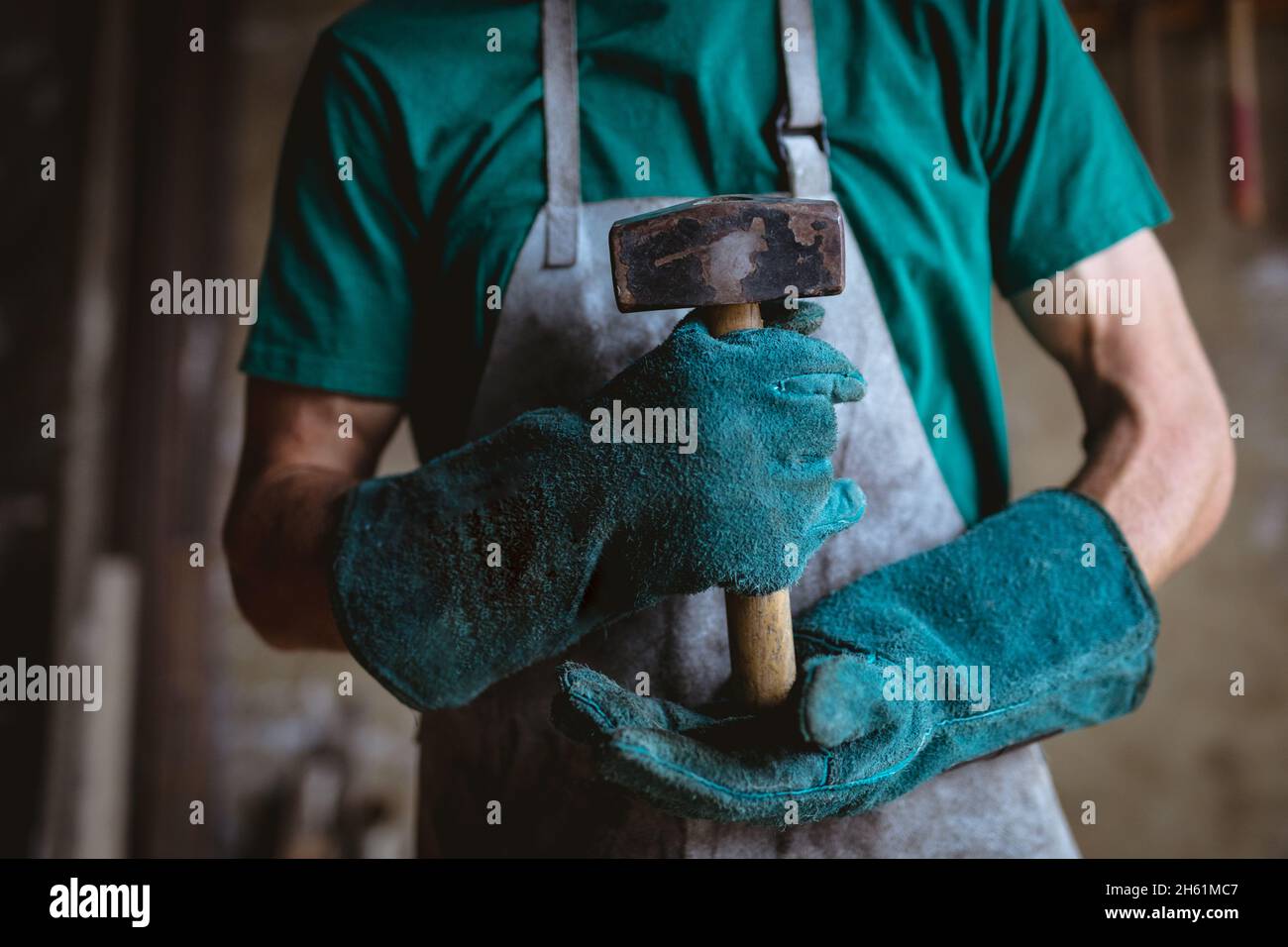 Mittelteil des Schmieds in schützender Arbeitskleidung, der Hammer hält, während er in der Industrie steht Stockfoto