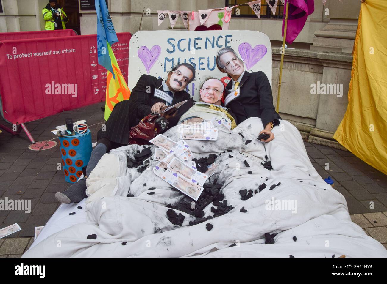 London, Großbritannien. November 2021. Demonstranten, die als Gautam Adani, der Direktor des Wissenschaftsmuseums Ian Blatchford und Shell-CEO Ben van Beurden gekleidet sind, liegen mit gefälschtem Geld und Kohle bedeckt im Bett. Demonstranten des Extinction Rebellion versammelten sich vor dem Science Museum in South Kensington, als Teil ihrer anhaltenden Proteste gegen die Unterstützung des Museums durch die fossilen Energieunternehmen Shell und Adani. Kredit: Vuk Valcic / Alamy Live Nachrichten Stockfoto