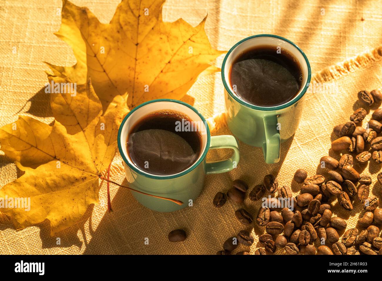 Tassen Kaffee und Kaffeebohnen, und gelbe Blätter durch Sonnenlicht beleuchtet , Herbsttag. Stockfoto