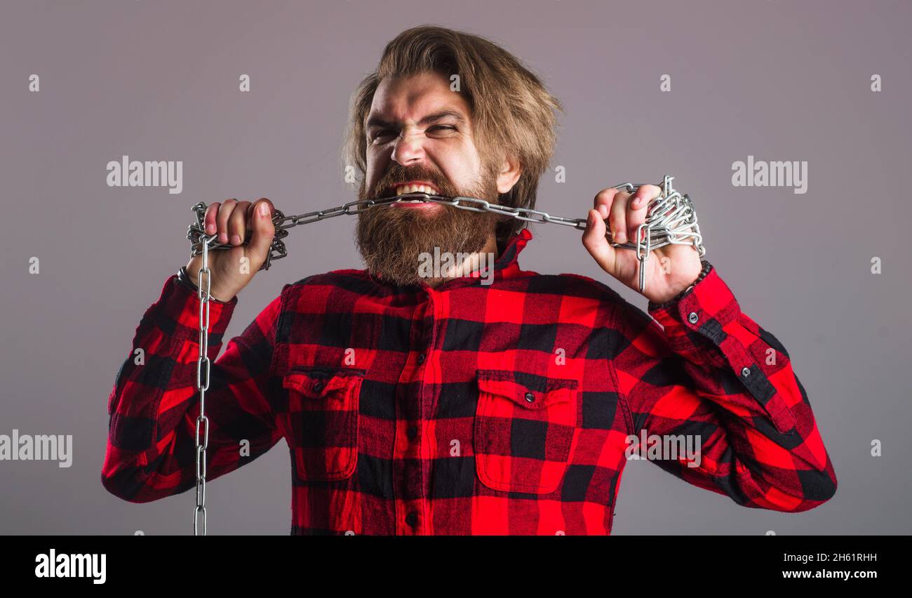 Mann reißt Metallkette an Zähnen. Freiheit. Bärtige Hipster-Kette. Starker Mann mit Ketten. Männermode. Stockfoto