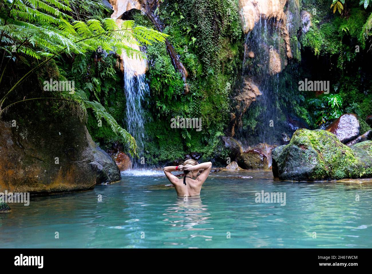 Frau im Badeanzug auf dem Hintergrund eines Wasserfalls in der Lagune, Frau im Thermalbecken von Caldeira Velha, Sao Miguel, Azoren, Portugal Stockfoto