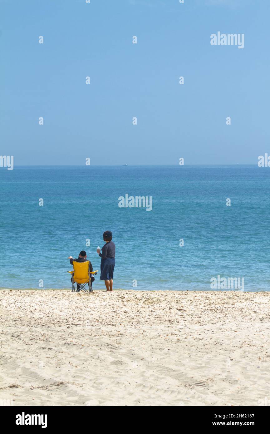 Jüdisches Paar, sitzender Mann und stehende Frau, am Hengistbury Head Beach mit Blick auf das Meer an Einem Summers Day, Christchurch, Großbritannien Stockfoto