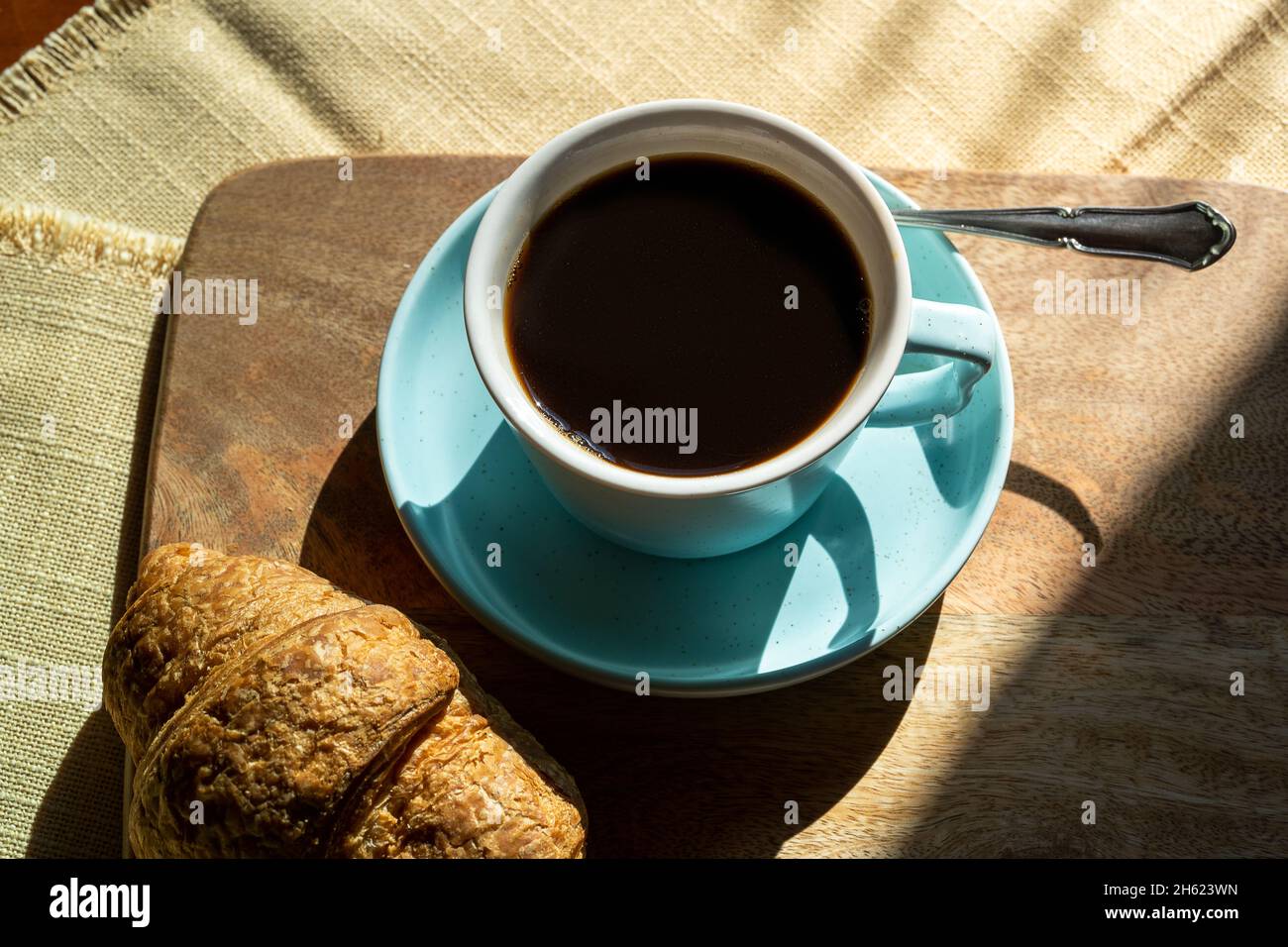 Tasse Kaffee und Croissant durch das Sonnenlicht beleuchtet, Herbsttag. Stockfoto