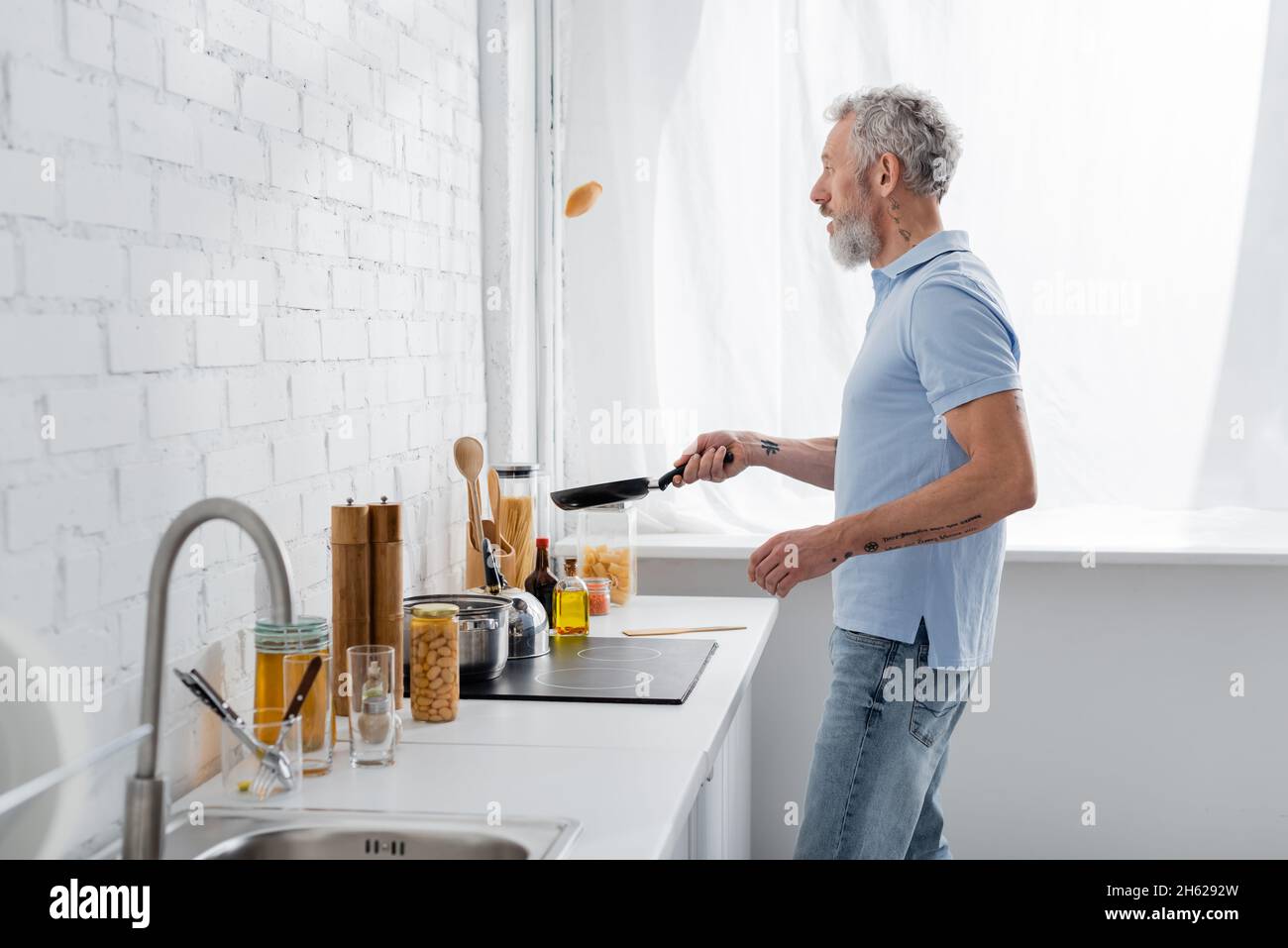 Seitenansicht eines reifen Mannes, der beim Kochen in der Küche Pfannkuchen warf Stockfoto