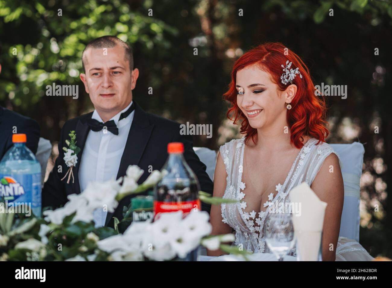 Glückliches, frisch verheiratetes Paar, das während ihrer Hochzeit am Esstisch saß Stockfoto