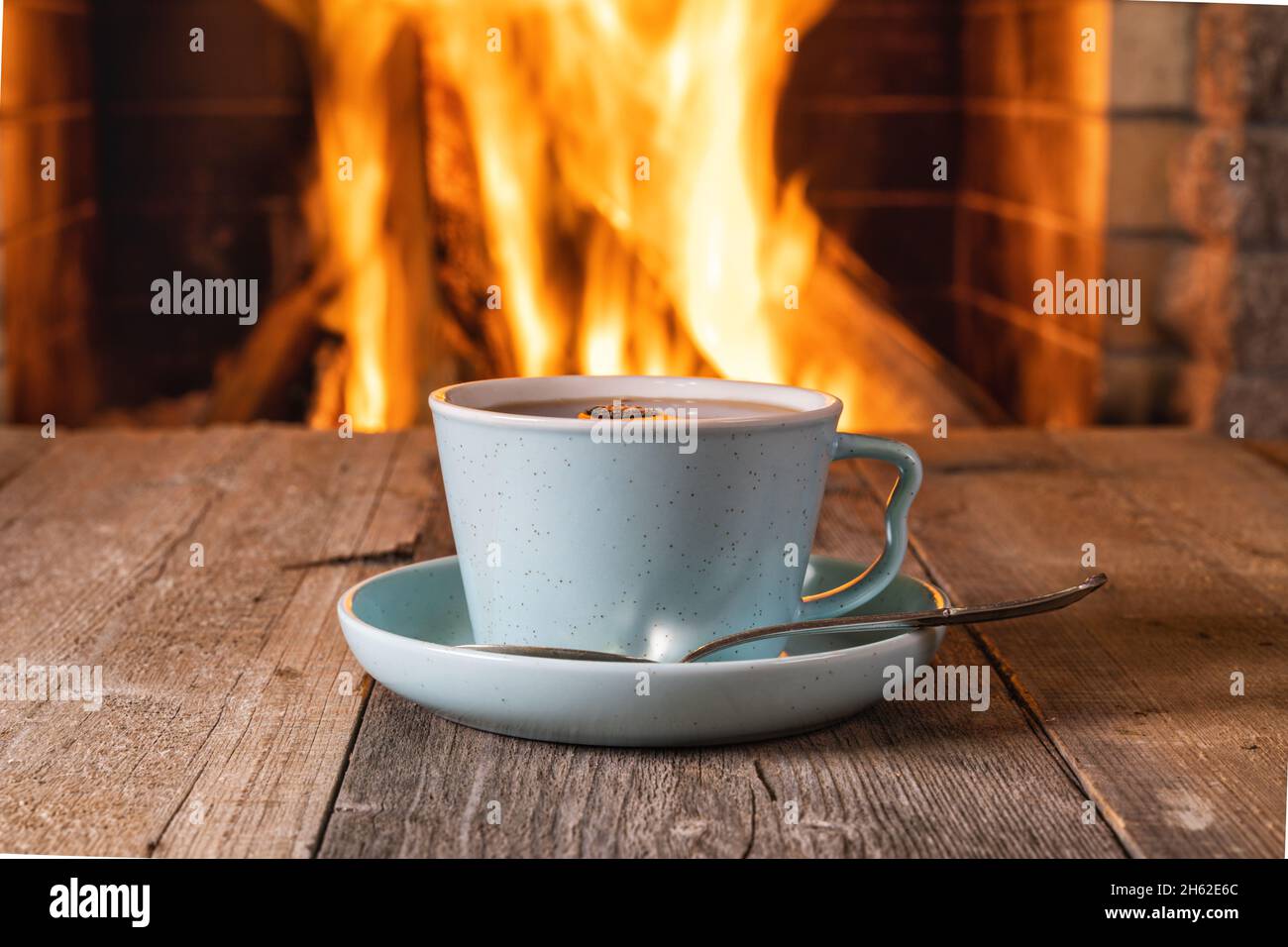 Tasse Tee oder Kaffeevor einem gemütlichen Kamin, in einem Landhaus, Herbst- oder Winterurlaub, horizontal. Stockfoto