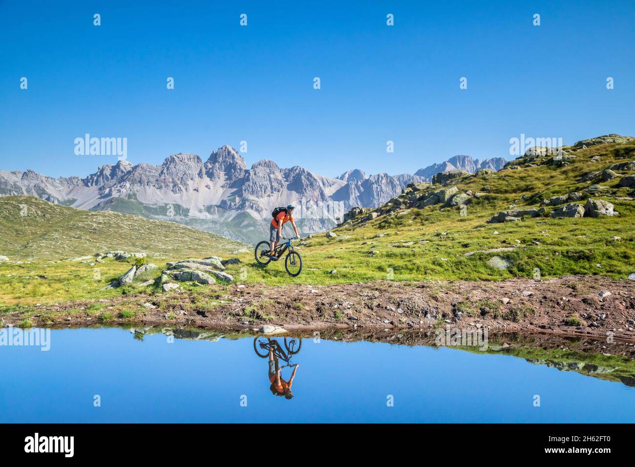 Mann, 22 Jahre alt, Radfahrer mit E-Bike in der Nähe eines alpinen Sees, Radfahrer im Wasser eines Bergsees reflektiert, Berge im Hintergrund. Laresei, falcade, belluno, veneto, italien Stockfoto