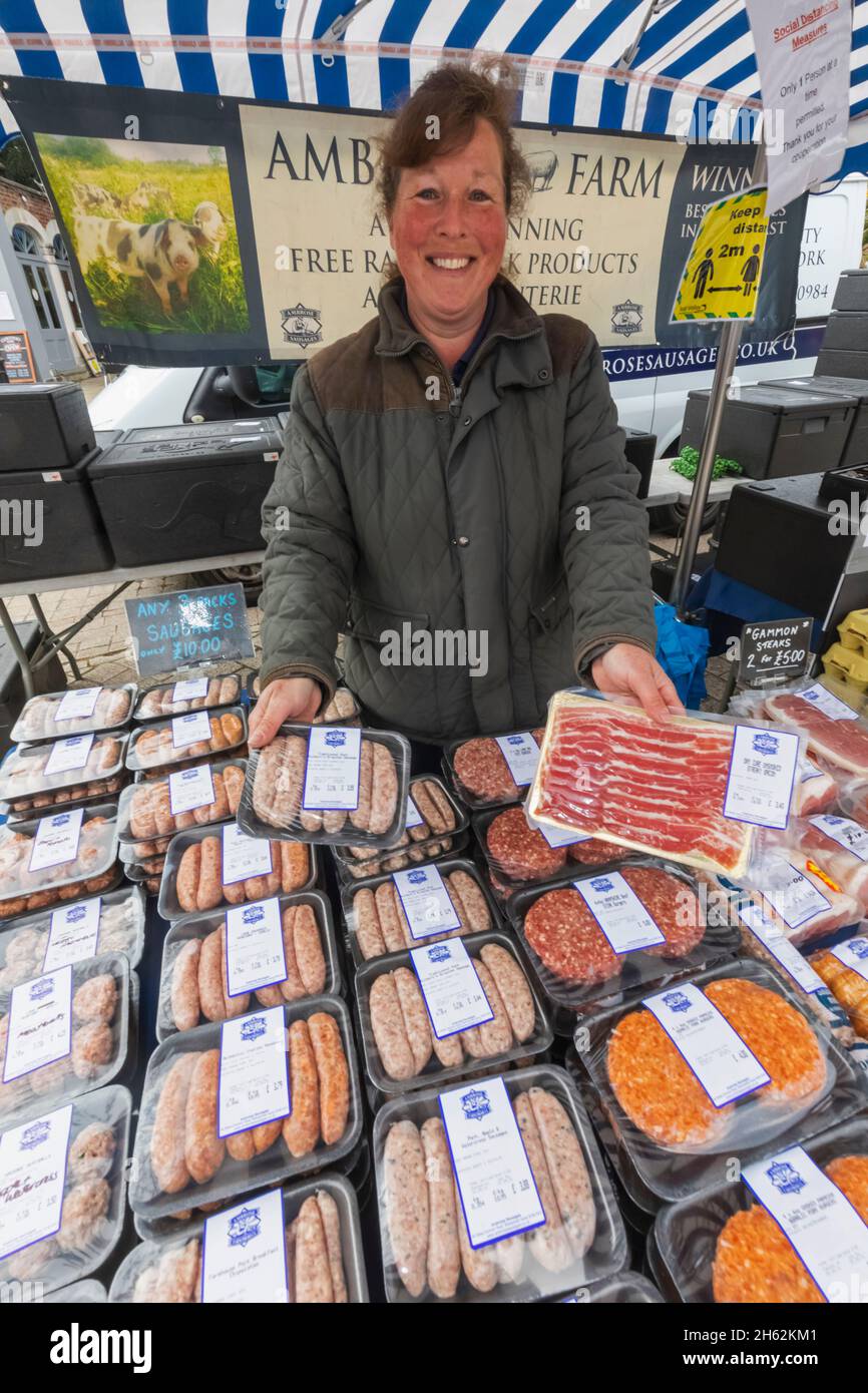 england, hampshire, petersfield, wöchentlicher Bauernmarkt, lächelnde Dame, die Fleischprodukte verkauft Stockfoto