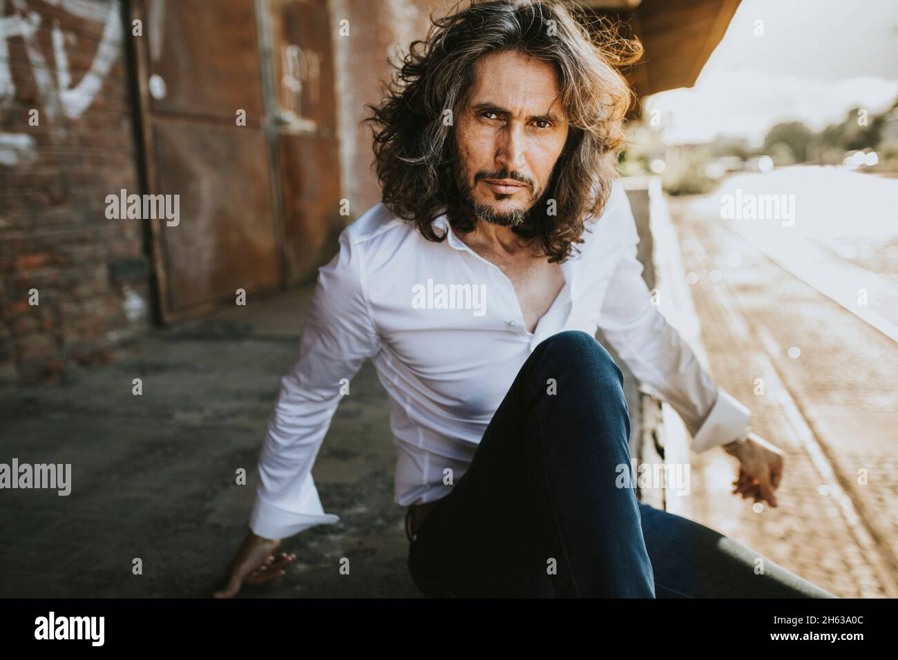 Ein charismatischer Mann mit Bart sitzt auf einem Güterbahnhof Stockfoto