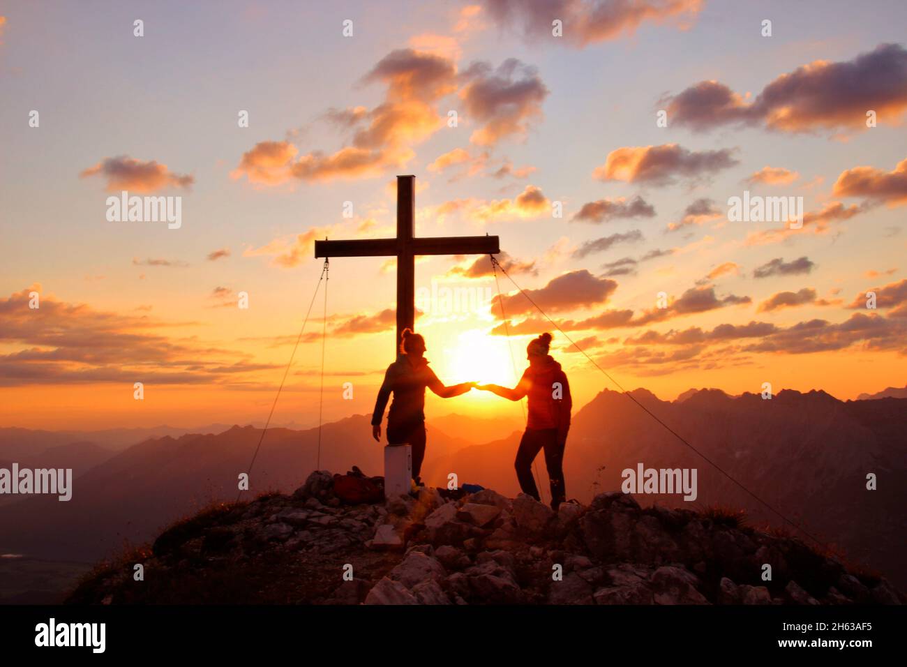 Zwei junge Frauen bei einer Wanderung,obere Wettersteinspitze,2.297 m,Gipfelkreuz,Klatschen,Sonne,Sonnenball,deutschland,bayern,oberbayern,werdenfelser Land,mittenwald,isartal Stockfoto