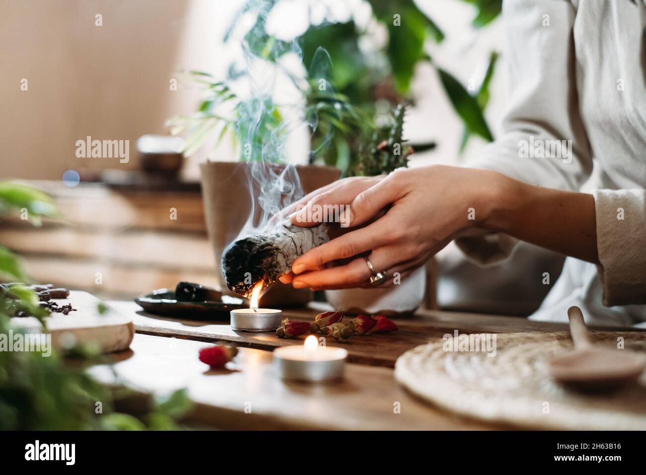 Frau Hände brennenden weißen Salbei, palo santo vor Ritual auf dem Tisch mit Kerzen und grünen Pflanzen. Rauch von Verschmierungen behandelt Schmerzen und Stress, klar Stockfoto