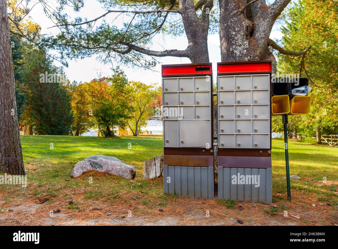 Alte Gemeindepostfächer entlang einer Straße an einem sonnigen Herbsttag ist Im Hintergrund Ein öffentlicher Park am Flussufer zu sehen. Stockfoto