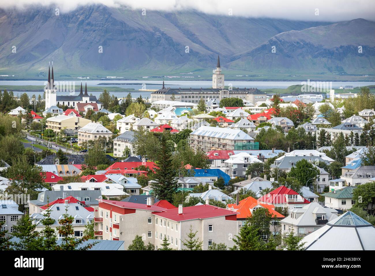 Farbenfrohe Dächer in einem Wohnviertel von Reykjavik an einem bewölkten Tag. Im Hintergrund sind hoch aufragende Küstenberge zu sehen. Stockfoto