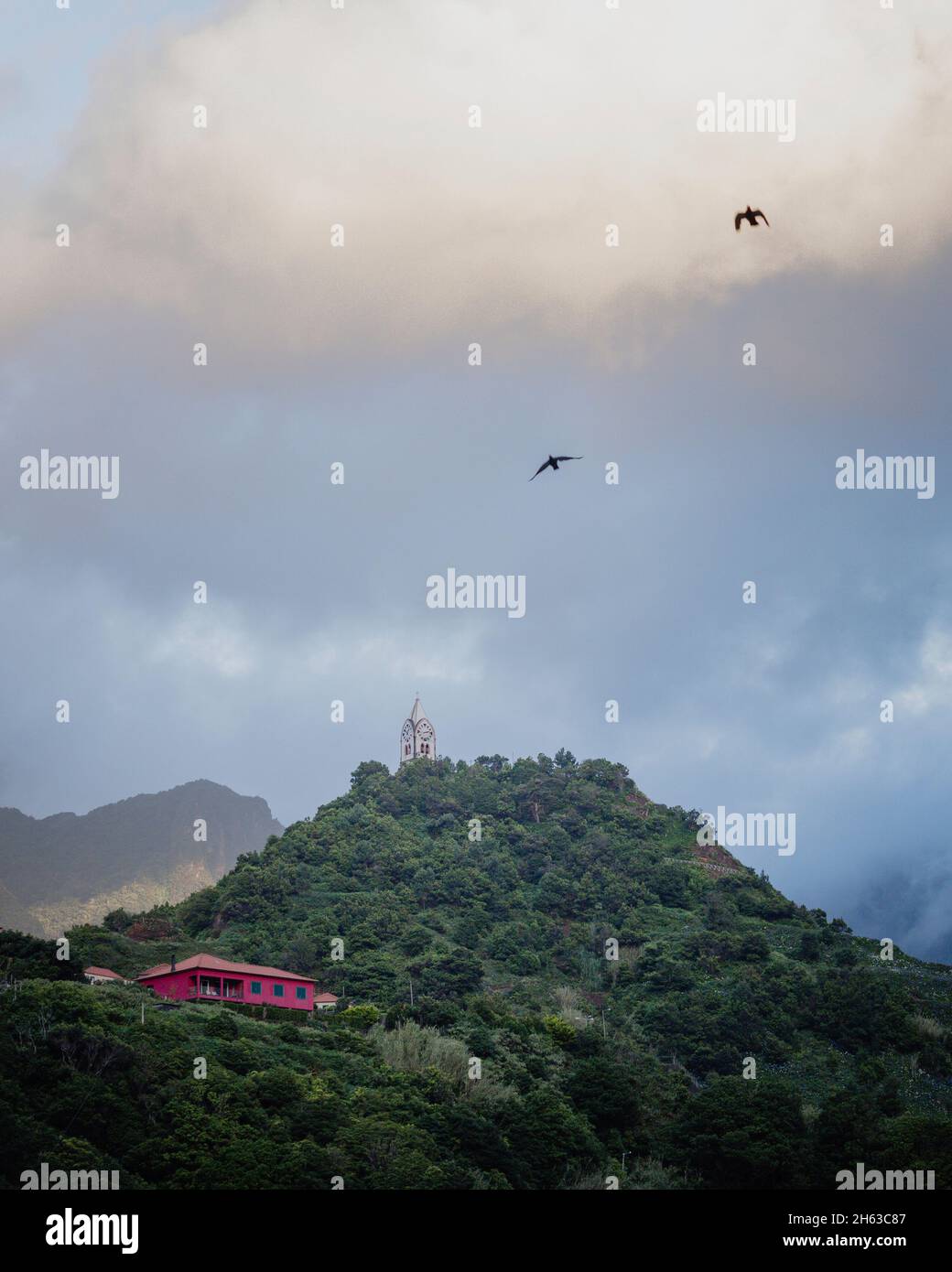 Abendhimmel auf madeira. Kapelle auf einem bewaldeten Hügel und 2 Vögel am Himmel. Stockfoto
