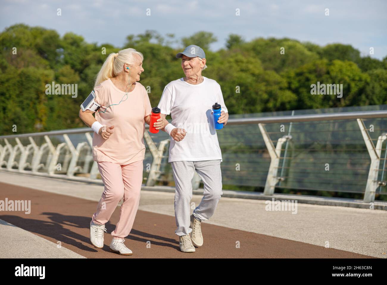 Glückliches Seniorenpaar mit Flaschen trainiert gemeinsam auf dem Steg Stockfoto