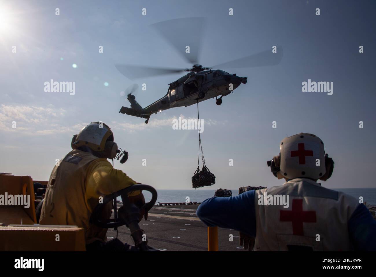 GOLF VON OMAN (NOV 11, 2021) Aviation Boatswain's Mate (Handling) Airman Corey Martin, Left, und Hospital Corpsman 3rd Class Kent Martin beobachten einen MH-60S Sea Hawk Hubschrauber, der an das Hubschrauber Sea Combat Squadron 21 angeschlossen ist, und legen Vorräte auf das Flugdeck des amphibischen Angriffsschiffs USS Essex (LHD 2) Während einer vertikalen Nachfüllung auf See mit dem Trocken- und Munitionsschiff USNS Cesar Chavez (T-AKE 14), November 11. Essex und die 11. Marine Expeditionary Unit werden im Einsatzgebiet der 5. US-Flotte eingesetzt, um Marinestützungen zu unterstützen, um die maritime Stabilität und Sicherheit in der CE zu gewährleisten Stockfoto