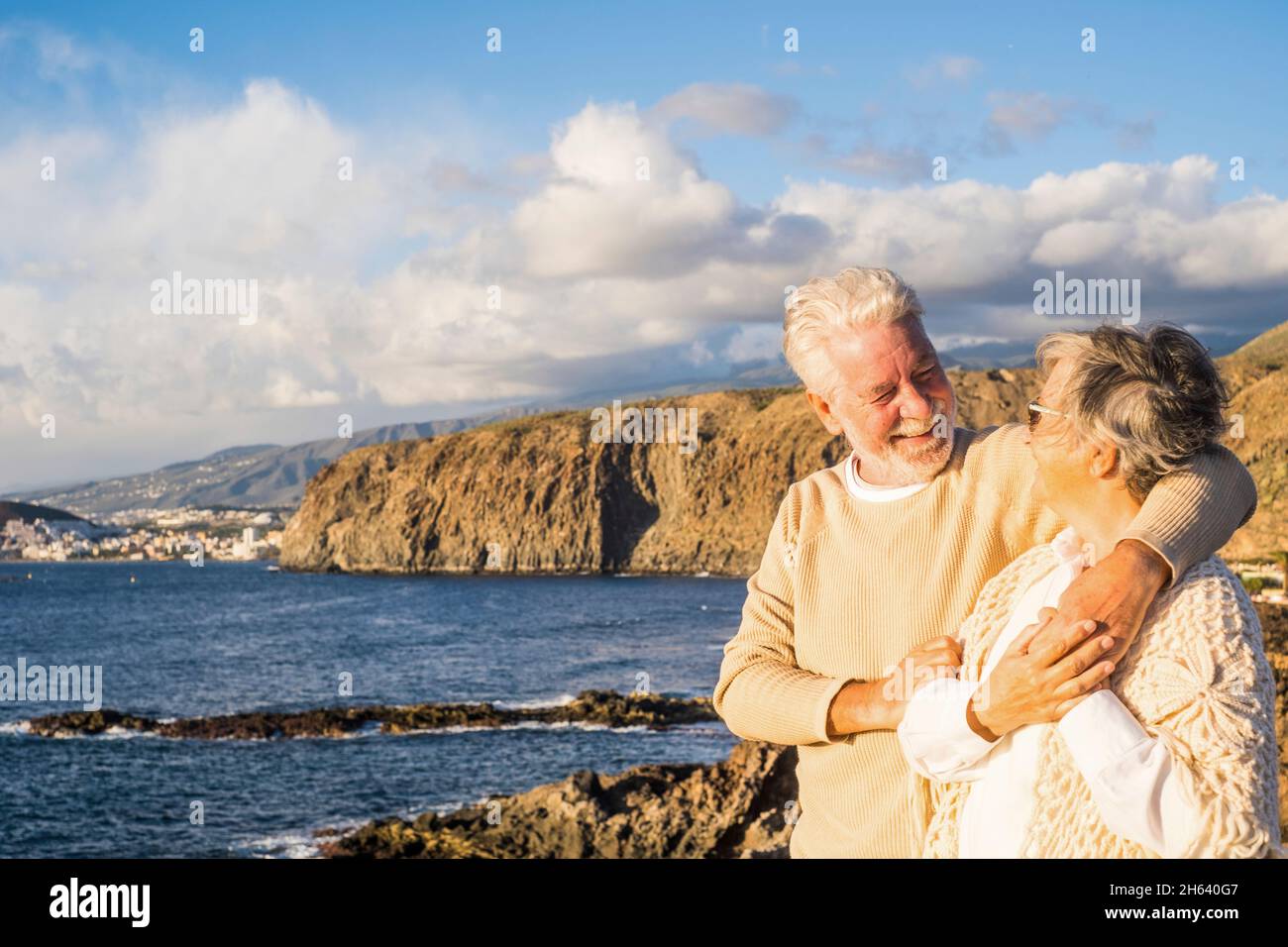 Portrait von ein paar älteren und älteren Menschen, die den Sommer am Strand genießen und lächelnd auf das Meer blicken und Spaß zusammen mit dem Sonnenuntergang im Hintergrund haben. Zwei aktive Senioren, die im Freien reisen. Stockfoto