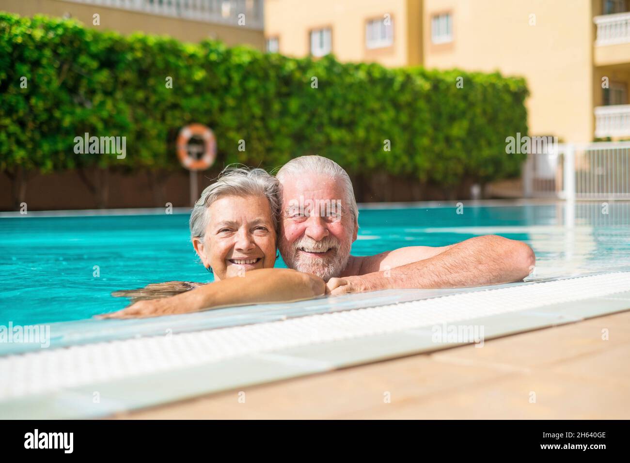 Ein paar von zwei glücklichen Senioren, die Spaß haben und gemeinsam im Schwimmbad genießen lächeln und auf die Kamera schauen. Glückliche Menschen genießen den Sommer im Freien im Wasser Stockfoto