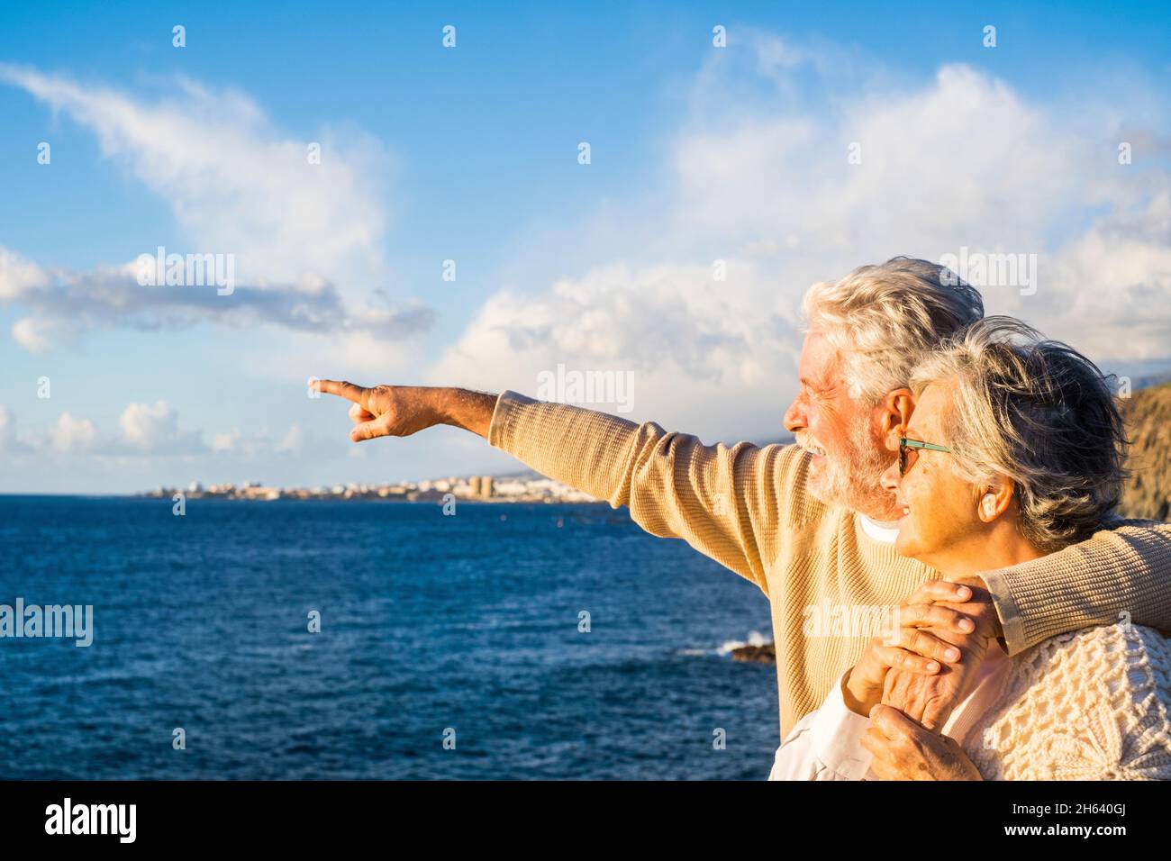 Portrait von ein paar älteren und älteren Menschen, die den Sommer am Strand genießen und lächelnd auf das Meer blicken und Spaß zusammen mit dem Sonnenuntergang im Hintergrund haben. Zwei aktive Senioren, die im Freien reisen. Stockfoto