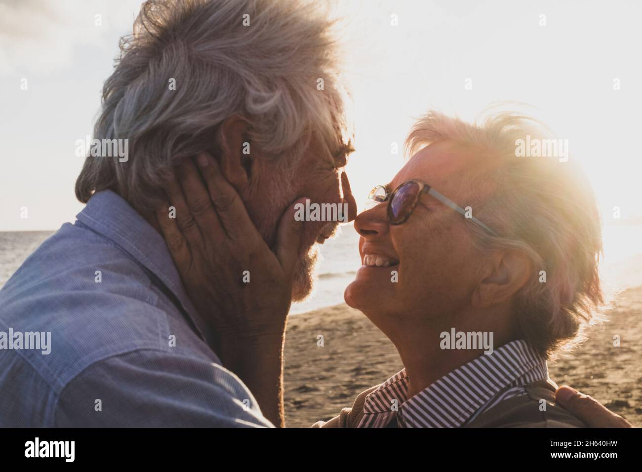 Porträt und Nahaufnahme von zwei verliebten Senioren, die lächelnd mit der Sonne des Sonnenuntergangs zwischen ihren Köpfen tanzen Stockfoto