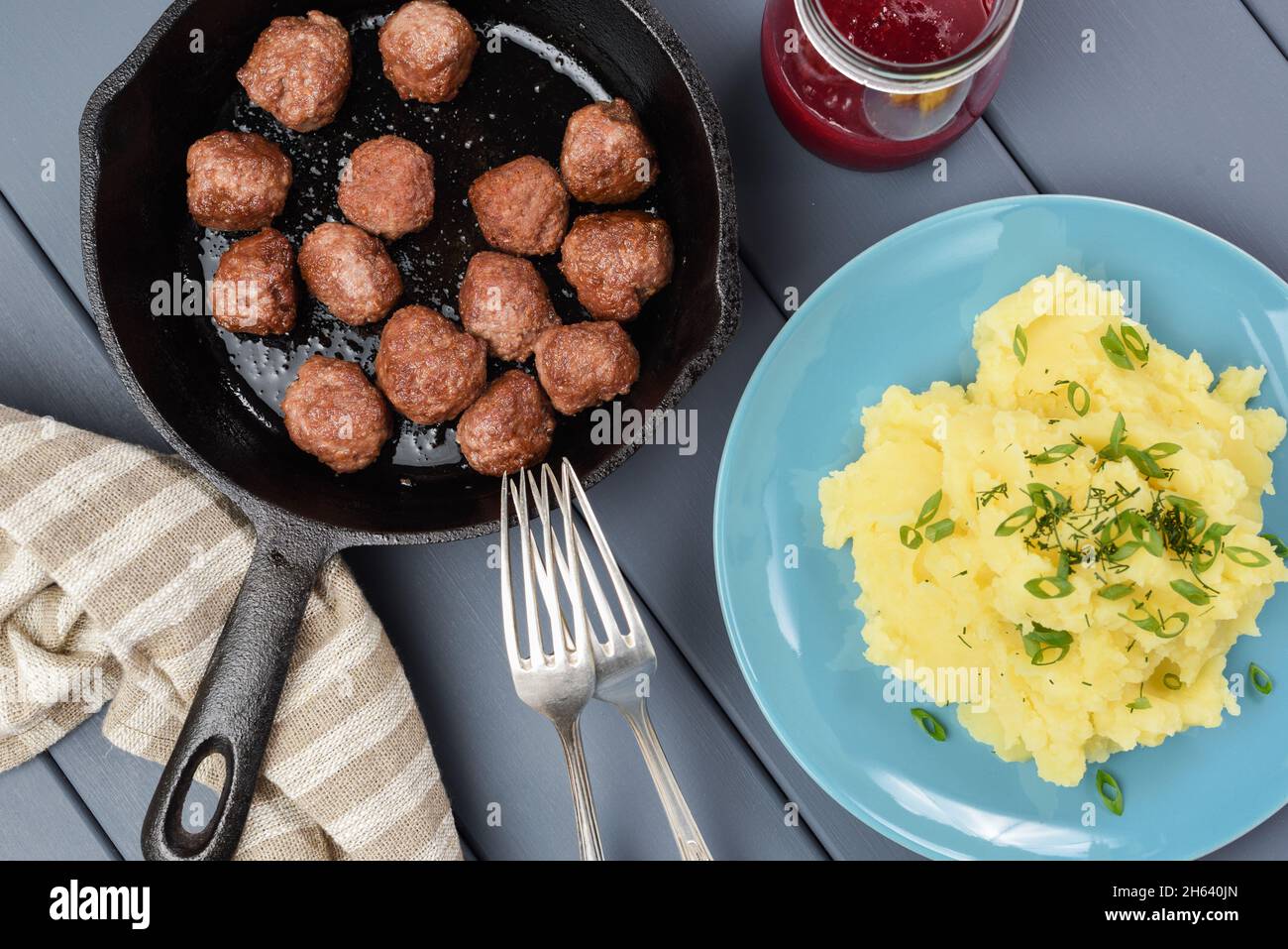 Hausgemachte, unperfekte Fleischbällchen, gebraten in einer gusseisernen Pfanne, Kartoffelpüree mit frischem Lauch und Preiselbeerensause. Skandinavische Küche mit Blick von oben Stockfoto