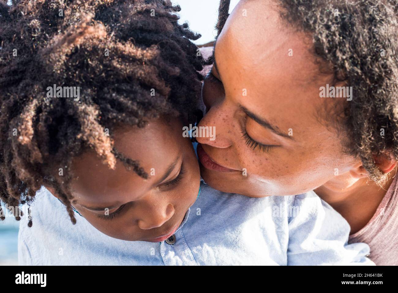Nahaufnahme von Mutter und Sohn in Liebesgefühl - schwarze ethnische junge Frau küssen ansehnliche afroamerikanische Kind - Süße Familie Paar Outdoor-Konzept - afrikanische und moderne Frisur Menschen Stockfoto
